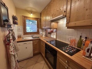A compact kitchen with wooden cabinets, a dishwasher, a stove, and a window with a view. - 3-Room Apartment in Méribel - Sleeps 6 (Méribel)
