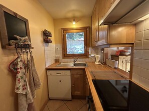 A compact kitchen with a dishwasher, a stove, and a window with a view of greenery. - 3-Room Apartment in Méribel - Sleeps 6 (Méribel)