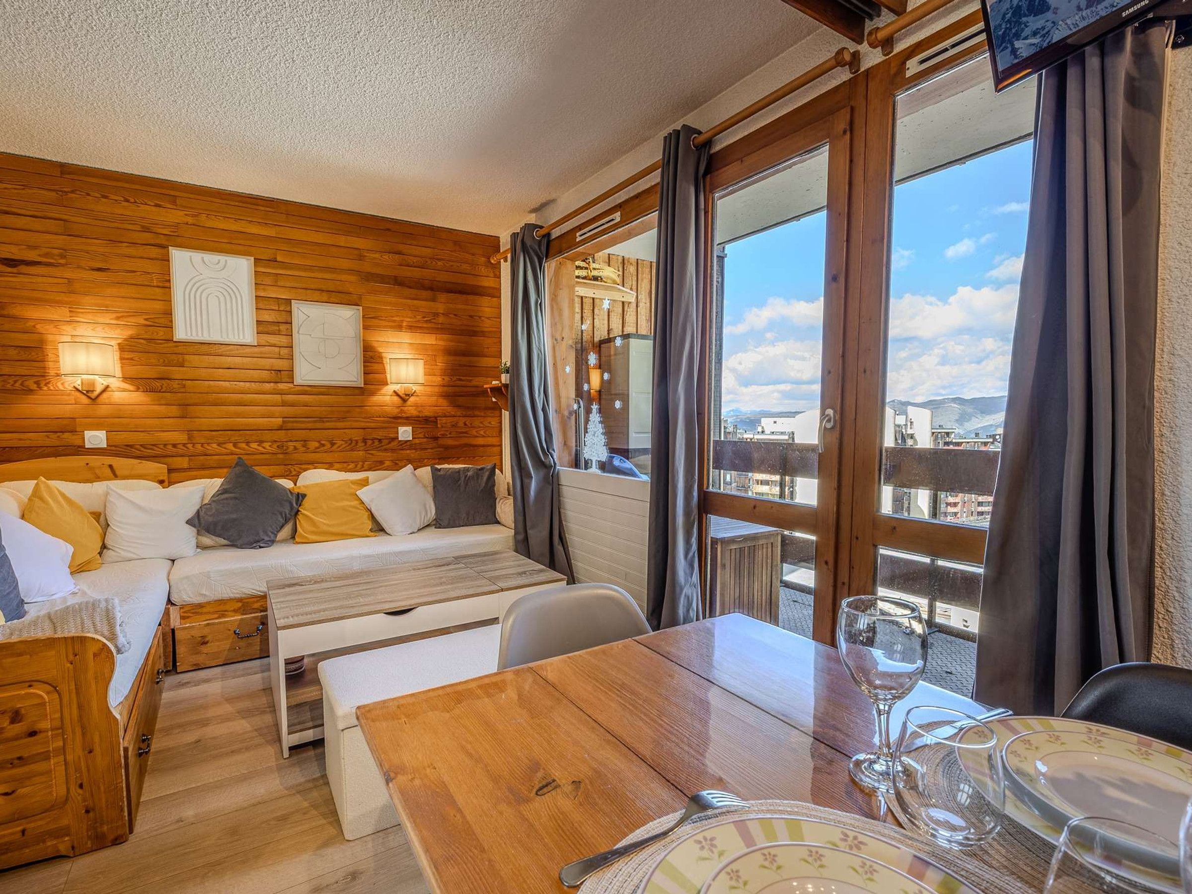 Een knus vertrek met een houten wand, een bed, een tafel met een glas en uitzicht op de stad.