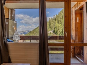 Eine Holzhütte mit großem Fenster, Metallgeländer und Blick auf Wald und Berge.