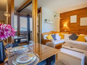 Ein Zimmer mit einem hölzernen Bett, einem Esstisch mit Tellern und Gläsern sowie Blick auf Berge durch eine offene Tür.