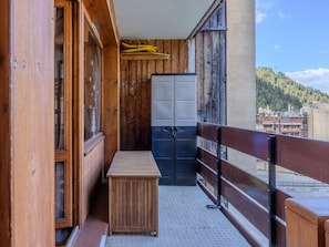 Ein schmaler Balkon mit Holzgeländern, einem kleinen Holztisch und einem Satz Doppeltüren.