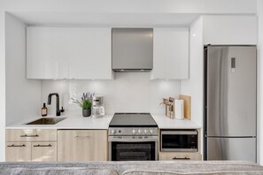 Une cuisine moderne dotée d’une cuisinière, d’un four et d’un réfrigérateur en acier inoxydable, de meubles blancs et d’un évier avec un robinet.