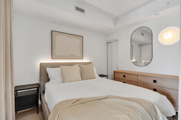 Une chambre à coucher comprenant un lit, des tables de chevet, une commode, un miroir et une œuvre d’art accrochée au mur.