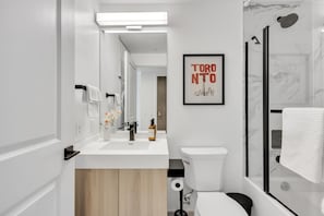 Une salle de bain moderne avec un lavabo, des toilettes et une douche, le tout de couleur blanche. Un tableau encadré représentant Toronto est accroché au mur.