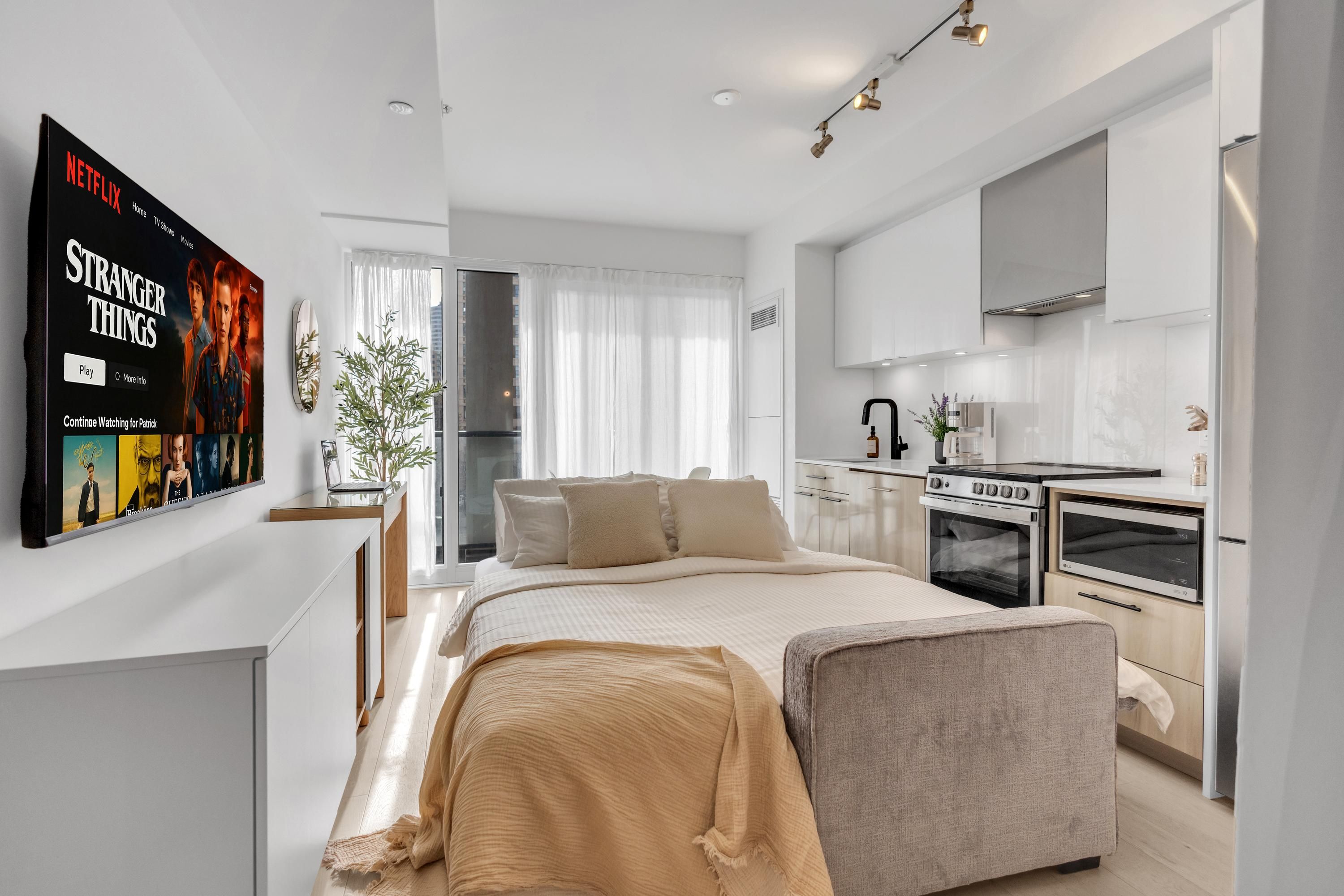 Un dormitorio moderno con una cama grande, una mesita de noche y un televisor mostrando una serie de Netflix.