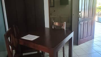 Un comedor con una mesa y sillas, una cocina visible a través de un ventanal, y piso de baldosas.