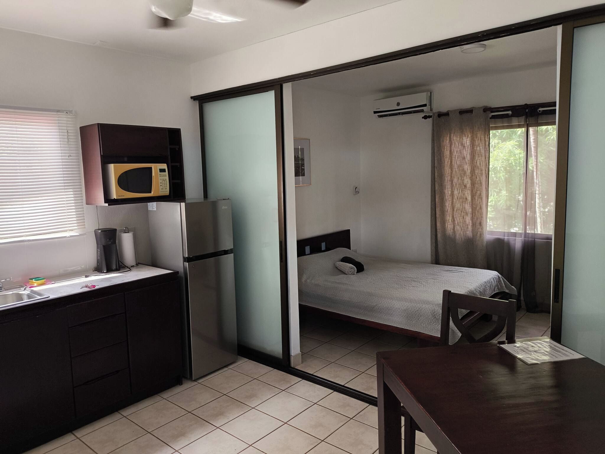 A compact room with a kitchenette, a bed, and a sliding door leading to a bathroom.