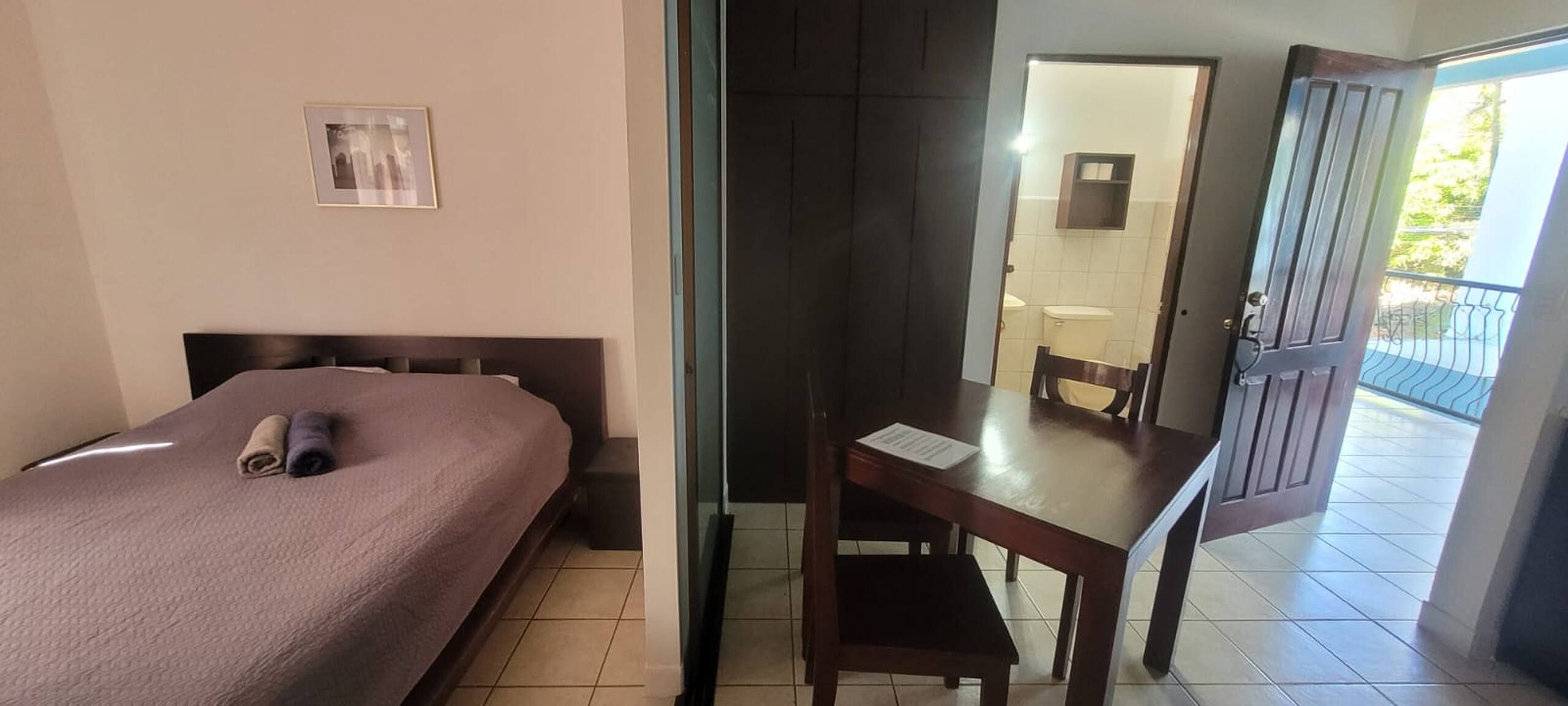Habitació d'hotel amb un llit, una taula de treball i un bany visible a través d'una porta oberta.