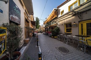A narrow street with buildings on either side, outdoor seating, and a sign for a shop. - Psiri Vibes Rooms & Suites in Athens (Athina)