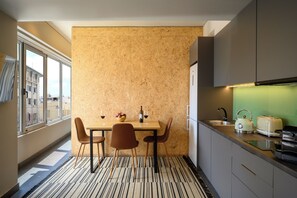 A compact kitchen with a dining area, featuring a wooden wall, modern appliances, and a view through the window. - Psiri Vibes Rooms & Suites in Athens (Athina)