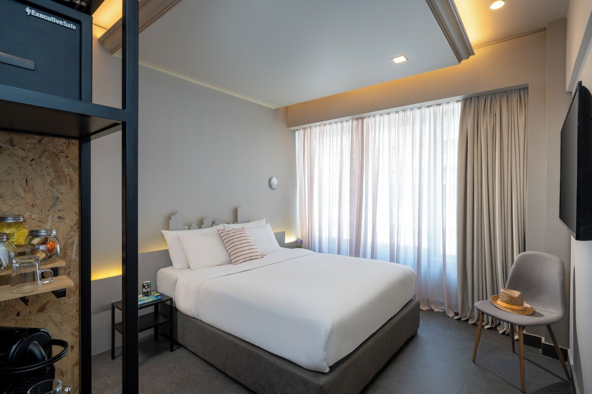 A hotel room with a large bed, a desk with a lamp, a chair, and a television.