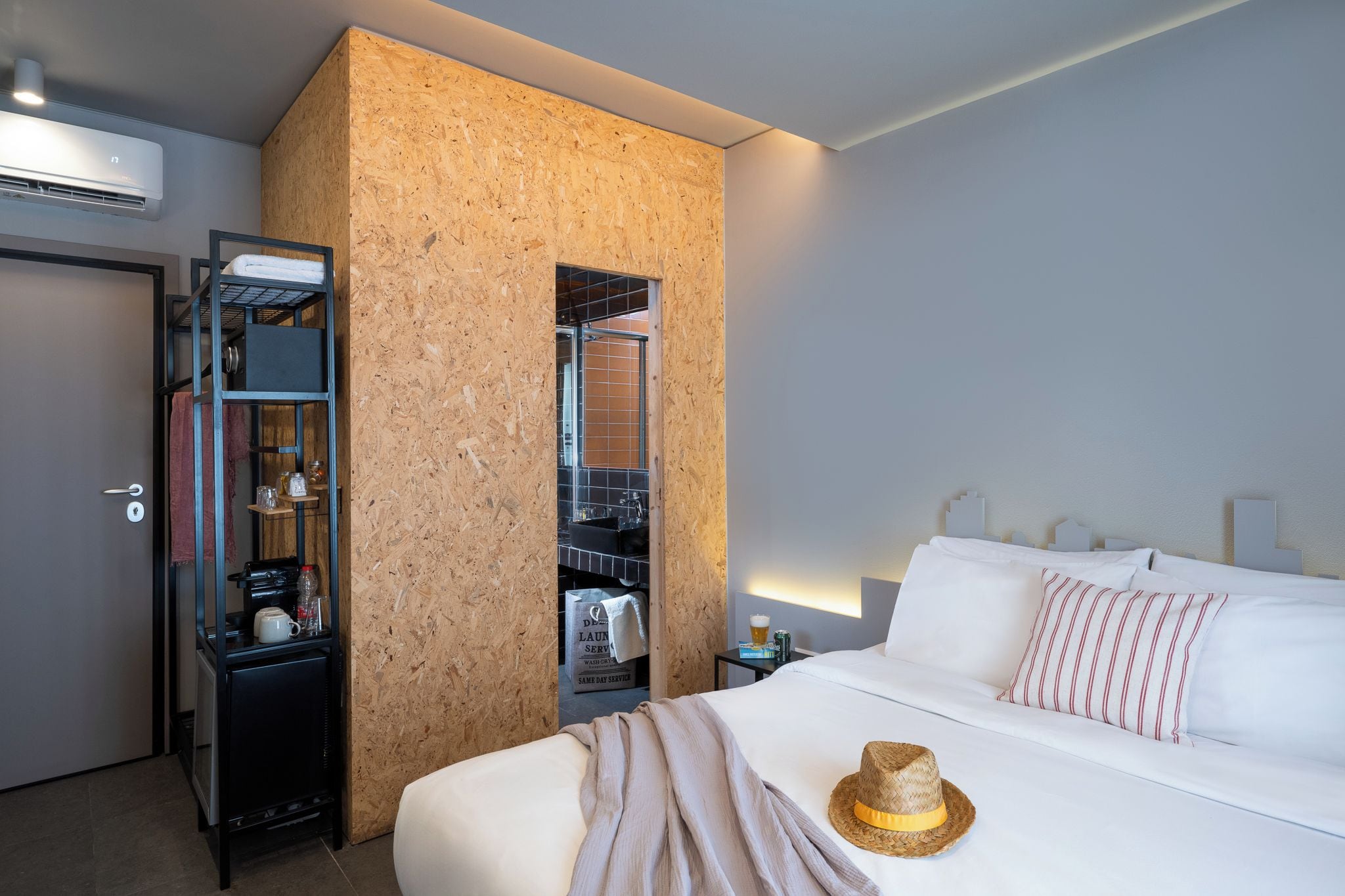 A hotel room with a bed, a wardrobe, a small table with a lamp, and a wall-mounted air conditioning unit.