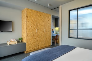 A modern bedroom with a large wardrobe, a bed, a desk with a chair, and a television mounted on the wall. - Psiri Vibes Rooms & Suites in Athens (Athina)