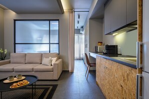 A modern living room with a sofa, a coffee table with pastries, and a view through a window with blinds. - Psiri Vibes Rooms & Suites in Athens (Athina)