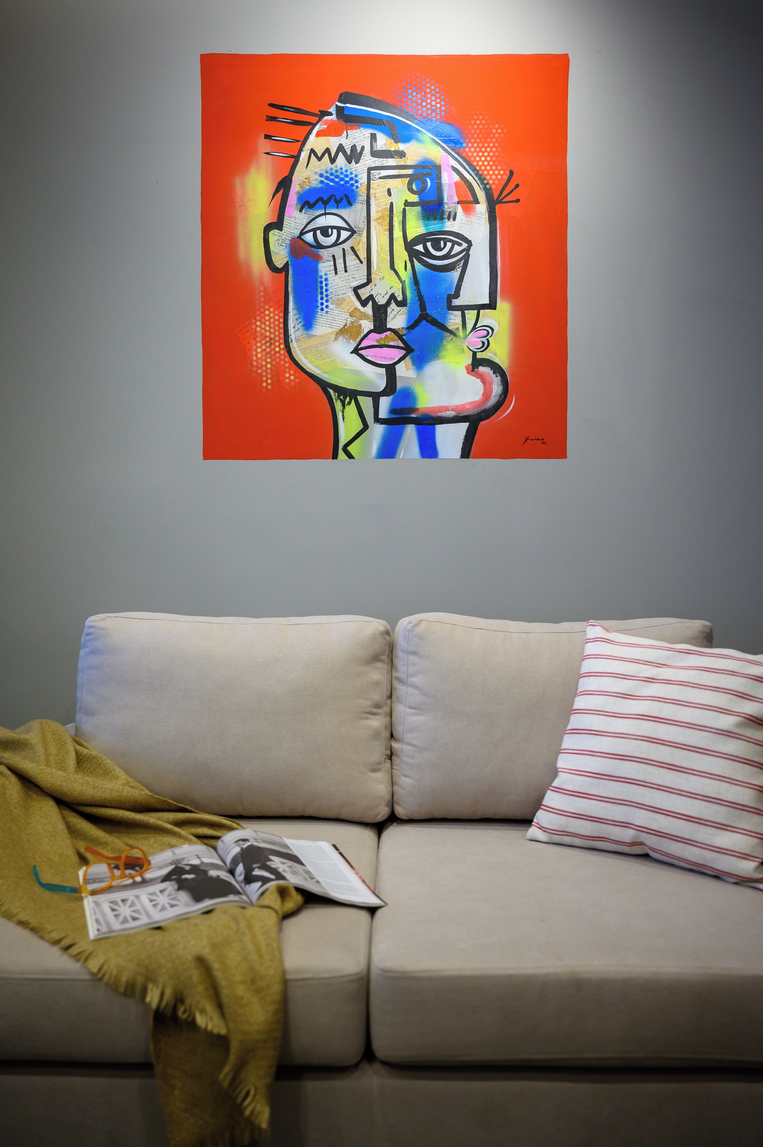 A living room with a beige sofa, a magazine, and a colorful abstract painting on the wall.