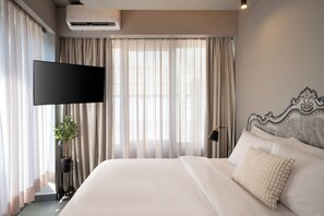 Ein Hotelzimmer mit einem großen Bett, einem flachbildfernseher an der Wand, einer Topfpflanze und einer Nachttischlampe.