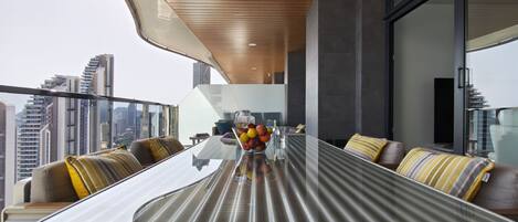 A modern dining area with a glass table, cushioned seating, and a city view.
