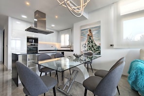 A modern kitchen with a glass dining table, grey chairs, and a stainless steel range hood. - SUNSET WAVES elegant apartment (Benidorm)
