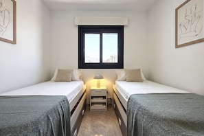 A twin room with two beds, a window, a nightstand with a lamp, and artwork on the walls. - SUNSET WAVES elegant apartment (Benidorm)