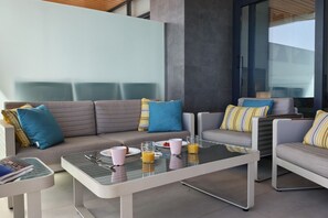 Un espace extérieur moderne, aménagé avec une table à plateau de verre, des canapés confortables et des coussins à rayures.