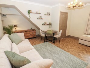 A living room with a sofa, a dining table with chairs, a staircase, and a door. - Corner House (Hexham)