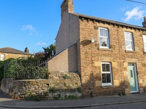 A two-story stone building with a green door, a satellite dish, and a stone wall with a fence. - Corner House (Hexham)