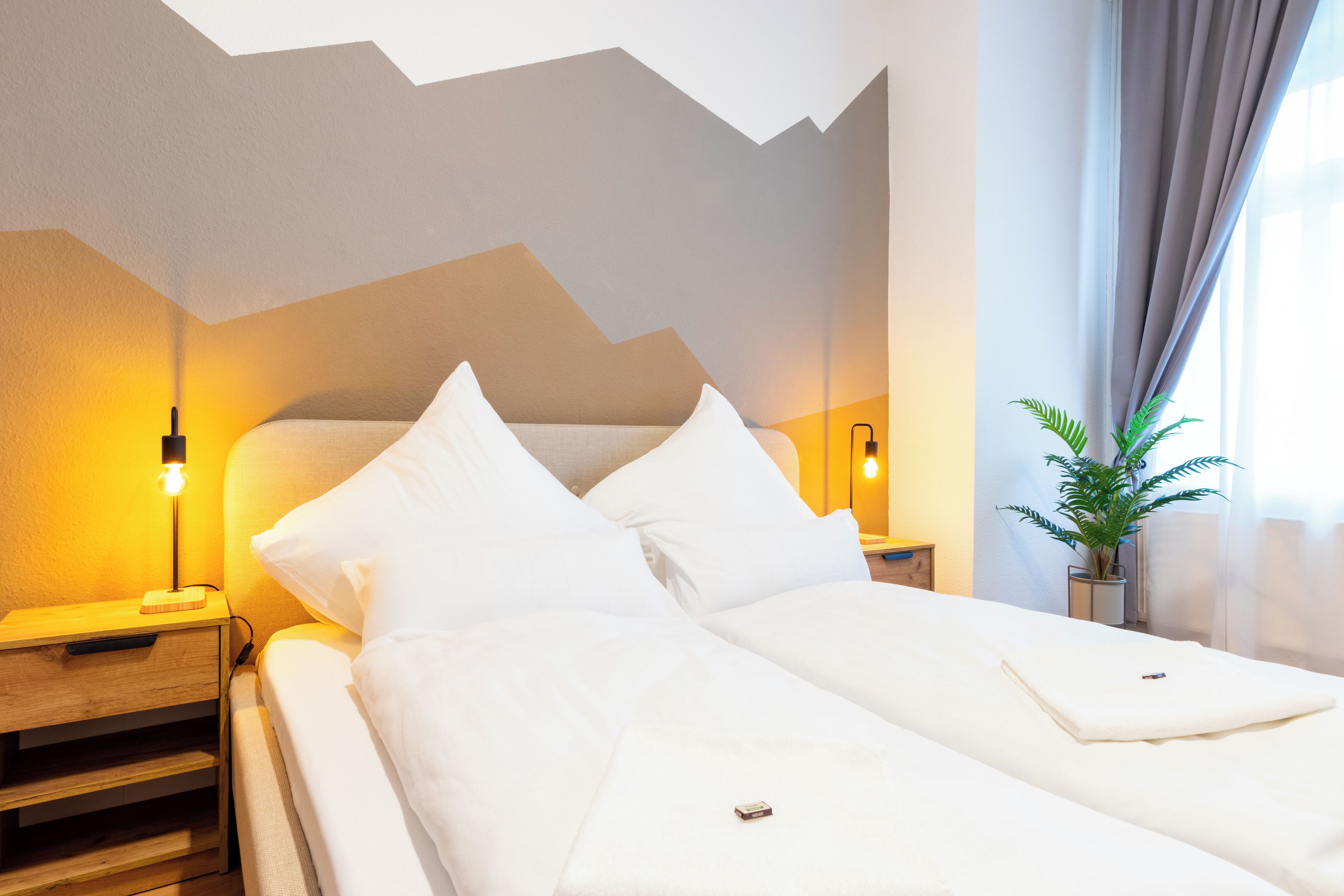 A hotel room with a bed, bedside lamps, a nightstand, and a potted plant.