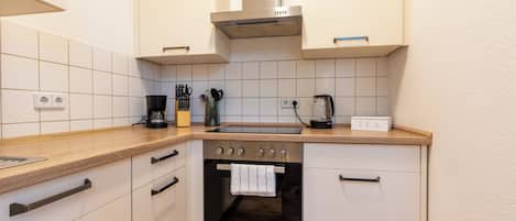 Una cocina compacta con horno empotrado, cafetera y hervidor sobre la encimera.
