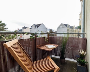 A wooden bench with a book on it, a potted plant, and a view of buildings in the background.
