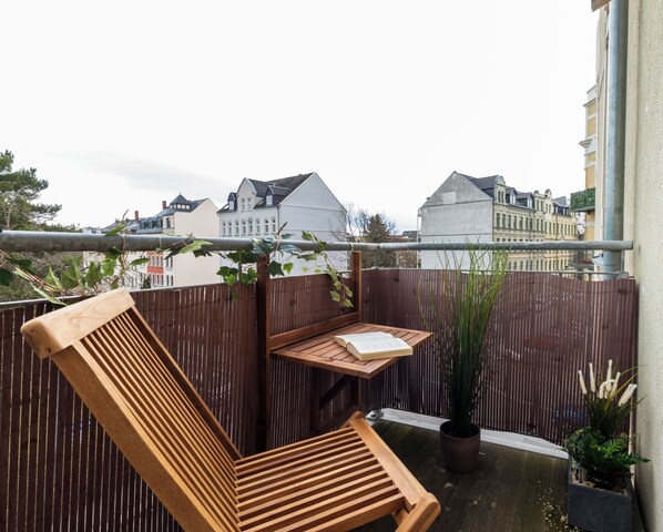 A wooden bench with a book on it, a potted plant, and a view of buildings in the background.