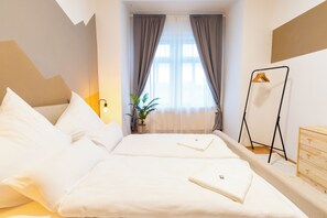 A hotel room with a bed, a bedside table, a hanging light, a potted plant, and a coat rack.