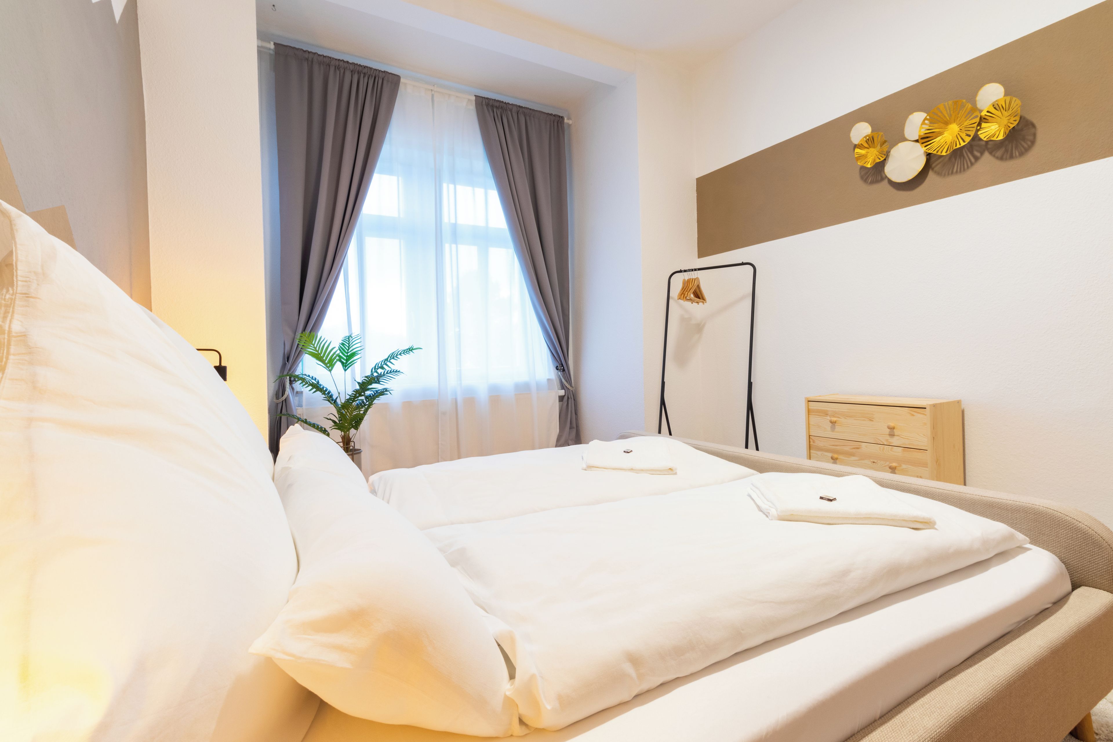 Een hotelkamer met een bed, nachtkastje, plant en een wandrek voor handdoeken.