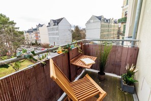Ein Balkon mit einem Holzstuhl, einem kleinen Tisch und einem Blumentopf.