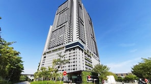 A high-rise building with multiple floors, surrounded by greenery and a clear sky.