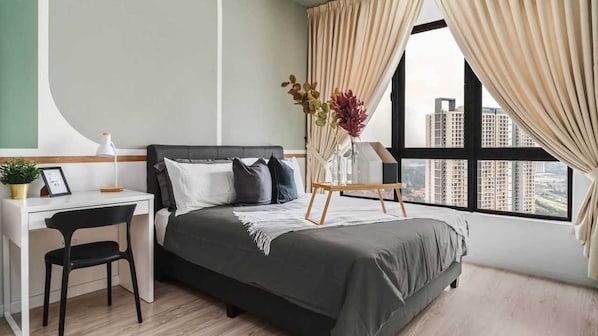 A modern bedroom with a bed, a desk, and a chair. There is a window with curtains, and a vase with flowers on a small table.