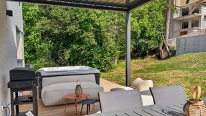 Een terras buiten met een jacuzzi, een houten terras en een tafel met stoelen.