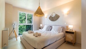 Een ruime slaapkamer met een groot bed, twee nachtkastjes met lampen, een ventilator en uitzicht op groen door het raam.