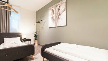 A hotel room with two beds, a nightstand, a lamp, a plant, and a painting on the wall.