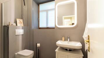 Ein modernes Badezimmer mit Toilette, Waschbecken, einem beleuchteten Spiegel, einem Fenster und einem Handtuchhalter.