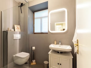 A modern bathroom with a toilet, a sink, a mirror with lights, a window, and a towel rack.