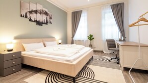 Ein Hotelzimmer mit Bett, Nachttischen, Schreibtisch, Stuhl, einer Pflanze und einem Fenster mit Vorhängen.