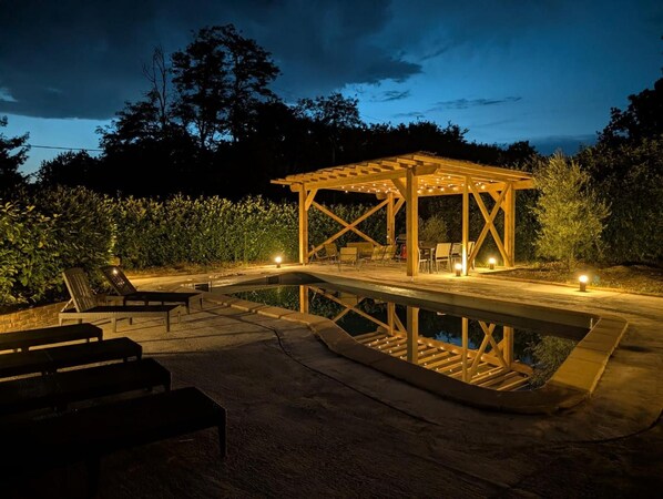 A wooden gazebo with string lights, a pool, and outdoor seating.