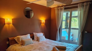 A bedroom with a bed, two wall-mounted lamps, a round mirror, and a view of an outdoor area through a window. - Villa 'Piscine 9pers SaôneBeaujolais' with Private Pool, Shared Terrace and Wi-Fi (Montmerle-sur-Saône)