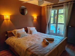 A bedroom with a bed, two wall-mounted lamps, a round mirror, and a view of an outdoor area through a window.