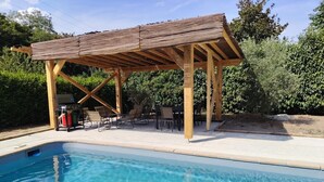 A pool area with a wooden pergola, lounge chairs, and a barbecue grill. - Villa 'Piscine 9pers SaôneBeaujolais' with Private Pool, Shared Terrace and Wi-Fi (Montmerle-sur-Saône)