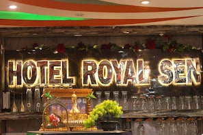 A bar area with a sign reading 'HOTEL ROYAL SEN' and a display of various bottles and glasses.