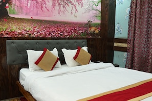 A bed with a grey upholstered headboard, white bedding, and two decorative pillows with red and beige accents.