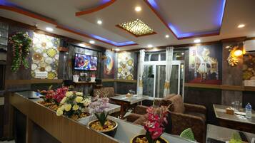 A restaurant interior with a counter, seating, decorative wall art, and a television.