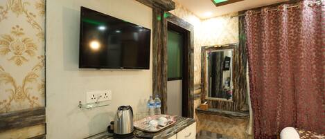 Habitación de hotel con televisor de pantalla plana en la pared, cafetera en la encimera, un espejo y una cama con un felpudo rojo.